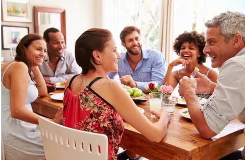 Group of six adults enjoying a casual meal together around a wooden dining table at home