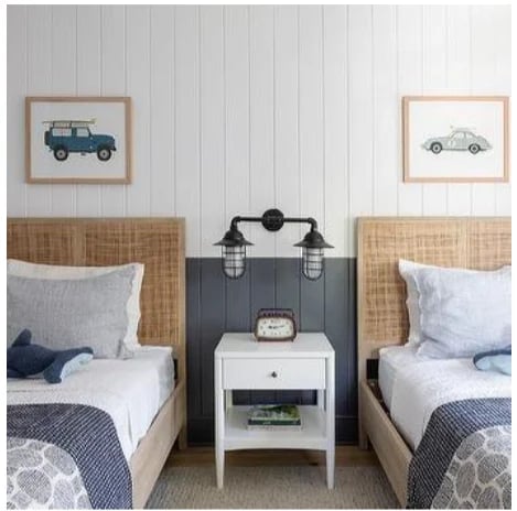 Twin bedroom with two single beds with rattan headboards, white nightstand between them, and framed vintage vehicle artwork on wall