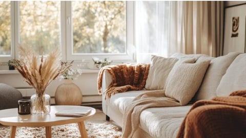 Bright living room with cream sofa, wooden table, pampas grass vase, and large windows overlooking trees